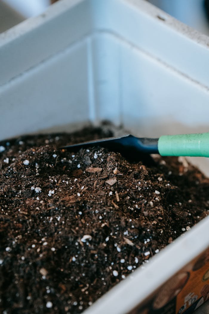 who-we-are Gardening soil with a green-handled trowel in a white container, perfect for planting.